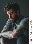 A man with tattoos sitting down and crossing his arms. Стоковое AI-изображение, AI-художник Данила Большаков / Фотобанк Лори