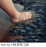 Oil spill or petroleum slick concept with the foot of a child walking on a sandy beach turned into a disaster zone with oily black sludge polluting the marine life as a man made catastrophe and environmental disaster symbol. Стоковое фото, агентство Ingram Publishing / Фотобанк Лори