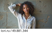 A black woman in a white blouse standing confidently with her arm raised against a textured stone wall, soft lighting enhancing. Стоковое AI-видео, аниматор Sergey Grishin / Фотобанк Лори
