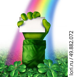 Saint Patricks day concept with a leprechaun hand in a green clover field holding up a blank white card as a rainbow glows upon the character as a symbol for spring and Irish celebration. Стоковое фото, агентство Ingram Publishing / Фотобанк Лори