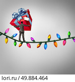 Holiday risk concept as a person holding a giant gift on a high wire tightrope made from christmas lights as a debt and credit metaphor and symbol of the challenges of giving. Стоковое фото, агентство Ingram Publishing / Фотобанк Лори