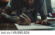 A man with tattooed arms focuses intently on writing a letter, the details of his tattoos visible as he works at a desk. Стоковое AI-изображение, AI-художник Данила Большаков / Фотобанк Лори