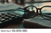 A pair of glasses resting on top of a calculator, with the numbers on the calculators screen visible. Стоковое AI-изображение, AI-художник Данила Большаков / Фотобанк Лори