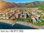 Aerial view of beautiful city. Aerial view of beautiful city, sandy beach with chaise-lounges, mountains, green trees, hotels, buildings, pool, at sunset in Icmeler, Turkey. Summer cityscape Top view from drone. Architecture. Стоковое фото, агентство Ingram Publishing / Фотобанк Лори