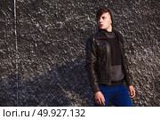 stylish young brunet in leather jacket standing near wall. Стоковое фото, агентство Ingram Publishing / Фотобанк Лори