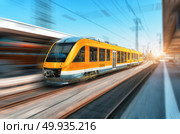 High speed orange train in motion on the railway station at bright day. Modern intercity train with motion blur effect on the railway platform. Industrial. Passenger commuter train on railroad. Travel. High speed orange train in motion on the railway station. Стоковое фото, агентство Ingram Publishing / Фотобанк Лори