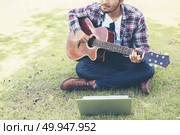 Young hipster man practiced guitar with laptop in the park,happy. Young hipster man practiced guitar with laptop in the park,happy and enjoy playing guitar. Стоковое фото, агентство Ingram Publishing / Фотобанк Лори