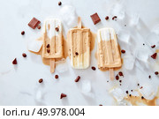 Vegan banana coffee creamy dairy free ice popsicles over ice and marble background with piece chocolate and coffee beans, top view. Homemade cold chocolate fudge popsicles on a stick over ice and marble background with piece chocolate and coffee beans, top view. Стоковое фото, агентство Ingram Publishing / Фотобанк Лори