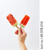 Watermelon ice lolly. Female hands holding juicy slices of watermelon on a stick on a white background with space for text.. A girl’s hand holds fresh organic slices of watermelon on a stick on a white background with copy space. The concept of summer cold dessert. Ice lolly. Стоковое фото, агентство Ingram Publishing / Фотобанк Лори