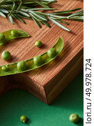 Fresh organic ingredients for preparing healthy vegetarian raw dieting food on a wooden board on a green. Detox dieting concept.. Opened sticks with green natural beans of peas and sprig of rosemary on a wooden cutting board on a green table. Стоковое фото, агентство Ingram Publishing / Фотобанк Лори