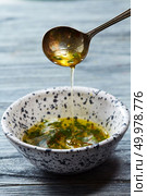 A homemade salad dressing with olive oil, chopped herbs and aromatic spices pours from a spoon into a bowl on a gray wooden background.. Ceramic bowl with freshly made natural sauce with spoon for salad from fresh organic vegetables on a gray wooden table. Стоковое фото, агентство Ingram Publishing / Фотобанк Лори