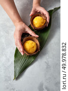The girl’s hands hold two coconut shells with mango ice cream balls on a palm leaf on a gray concrete background with a copy of the space. Top view. Female hands hold a coconut shell with yellow ice cream balls on a green leaf on a gray concrete background. Top view. Стоковое фото, агентство Ingram Publishing / Фотобанк Лори