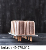 Coffee natural homemade ice-cream lolly in plastic forms on a black wooden table with space for text. Cold summer dessert. Cold dessert, coffee ice cream on a stick in the molds on a dark wooden table with copy space. Стоковое фото, агентство Ingram Publishing / Фотобанк Лори