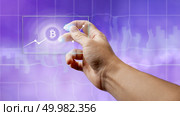 A businessman holds a glass screen with a bitcoin symbol and a crypto currency graph on the ultraviolet background of the city. Business, Finance and technology concept can be used for video or site cover. A man holds a glass screen with a bitcoin symbol and a crypto currency graph. Стоковое фото, агентство Ingram Publishing / Фотобанк Лори