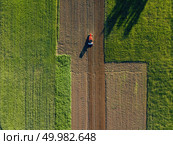 Abstract geometric forms of agricultural fields with different crops and soil without crop sowing, separated by road and tractor on it, in green and black colors with shadows from trees. A bird’s eye view from the drone.. Aerial view from the drone, a bird’s eye view of agricultural fields with a road through and a tractor on it in the spring evening at sunset in the summer. Стоковое фото, агентство Ingram Publishing / Фотобанк Лори