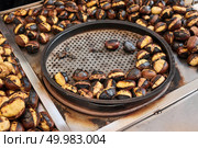 Fried chestnuts on the street. Street food. Roasted chestnuts served in a special perforated chestnut pan.. Grilled chestnuts for sale on street. Стоковое фото, агентство Ingram Publishing / Фотобанк Лори