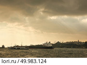 View of the old historical building with mosques, towers, buildings in the eastern style, cargo ships, tugboats in the port on the roadstead on the background of cloudy sky.. Landscape panoramic view from the sea to the historical part of Istanbul, Turkey. Стоковое фото, агентство Ingram Publishing / Фотобанк Лори