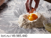 A woman holds an egg shell against a background of flour with yolks. Preparation of the dough. Стоковое фото, агентство Ingram Publishing / Фотобанк Лори