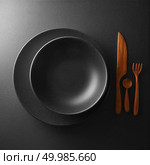 food concept - top view of black plate with knife, spoon and knife on dark table. serving of black table with dark wooden utensils and cutlery. Стоковое фото, агентство Ingram Publishing / Фотобанк Лори