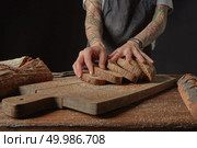 On a wooden cutting board a Woman with tattoos on her hands holding sliced pieces of fresh bread. Baker Holds Bran Bread. Стоковое фото, агентство Ingram Publishing / Фотобанк Лори