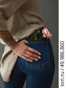 Young woman with tatoo hand and pink rose media in her pocket. View from the back. Against a gray background. Mother’s Day, Valentine’s Day. Woman with pink rose media in her pocket. Стоковое фото, агентство Ingram Publishing / Фотобанк Лори