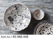 Porcelain gray bowls and plates on a gray wooden table with place for text. Colorful ceramic vintage handmade dishes. Flat lay. Decorative pottery - bowls, plates covered with glazed on a gray wooden background. Top view of traditional handcrafted. Стоковое фото, агентство Ingram Publishing / Фотобанк Лори