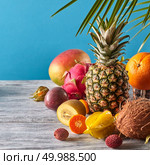 Group of exotic tropical fruits. Mango, dragon fruit, passion fruit, coconut, pineapple, carambola, kumquat on a blue background with copy space. Vegetarian healthy concept.. Exotic mix from ripe fruits - pineaple, dragon fruit, mango, coconut, kiwi, carambola, litchi on a gray wooden table on a blue. Стоковое фото, агентство Ingram Publishing / Фотобанк Лори