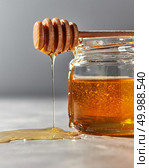 Dripping sweet flower honey from dipper above the glass pot with dessert on a gray stone background, copy space. Traditional healthy sweetness.. Close-up of natural sweet flower honey dripping from stick on a gray stone table. Rosh hashanah jewish holiday concept. Стоковое фото, агентство Ingram Publishing / Фотобанк Лори