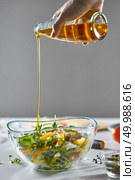 A girl’s hand pours oil into a freshly prepared vegetable salad in a bowl on a gray background with copy space. Healthy food. On the kitchen table was a bowl with a healthy salad. A woman’s hand pours oil into a salad on a gray background with a copy space. Стоковое фото, агентство Ingram Publishing / Фотобанк Лори