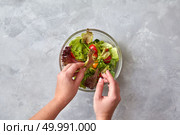 woman is preparing a salad of fresh vegetables on a gray background. Step-by-step recipe, a cooking step of a salad. Top view, flat lay.. woman prepares vegetable salad. Стоковое фото, агентство Ingram Publishing / Фотобанк Лори