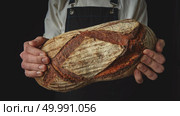 The baker’s hands hold a fresh organic oval bread on a black background , cloes up. Baker’s hands hold an oval bread. Стоковое фото, агентство Ingram Publishing / Фотобанк Лори