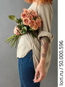 Woman in blue jeans and tatoo hand with a bouquet of beige roses cappuccino on a gray background. Mother’s Day,. Woman in blue jeans with a bouquet of beige roses. Стоковое фото, агентство Ingram Publishing / Фотобанк Лори