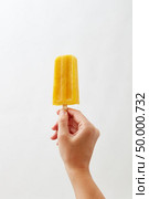 Cold natural yoghurt ice popsicle , holds a female hand on a white background with space for text. A photo can be used for your business ideas. A woman’s hand holds a yellow yoghurt ice cream lolly on a white background with copy space. Healthy food. Business concept concept. Стоковое фото, агентство Ingram Publishing / Фотобанк Лори