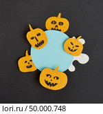 Decorative application handcraft from paper with terrible yellow pumpkins smiling on a blue round frame on a black background, place for text. Halloween concept. Flat lay.. Creative Halloween handmade blue frame with paper horrible smiling and laughing pumpkins on a black paper background. Стоковое фото, агентство Ingram Publishing / Фотобанк Лори