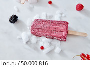 Berry apetitic organic ice cream lolly is represented on a gray marble table with different berries and ice cubes with a copy of the space. Ice cream on a blackberry stick with ice cubes, raspberry and red currant berries on a gray marble background with space for text. Healthy dessert. Flat lay. Стоковое фото, агентство Ingram Publishing / Фотобанк Лори