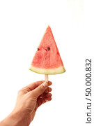 A man’s hand holds a juicy piece of watermelon lolly on a white background with space for text. The concept of fruit ice cream. A triangular slice of a watermelon on a stick to hold a male hand on a white background with copy space. Conception of berry ice cream. Стоковое фото, агентство Ingram Publishing / Фотобанк Лори