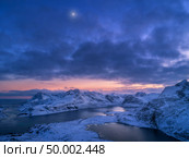 Aerial view of snowy mountains, sea, colorful cloudy sky at night in Lofoten islands, Norway. Winter landscape with snow covered rocks and seacoast and sunset sky. Top view of Norwegian Fjords at dusk. Стоковое фото, агентство Ingram Publishing / Фотобанк Лори