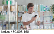 Adult man taking pictures with mobile medicated shampoo against hair loss in pharmacy. Customer scans a shampoo barcode at a pharmacy. Стоковое видео, видеограф Яков Филимонов / Фотобанк Лори