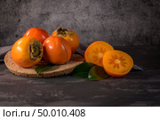 Ripe persimmon fruits in a cork plate on dark kitchen counter top. Стоковое фото, агентство Ingram Publishing / Фотобанк Лори