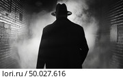 A man wearing a black suit and hat stands in the dimly lit alley, casting shadows around him. Стоковое AI-изображение, AI-художник Данила Большаков / Фотобанк Лори