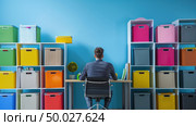 A person is sitting at a desk in front of a bookcase, engrossed in reading or studying. Various books are neatly arranged on the shelves behind them. Стоковое AI-изображение, AI-художник Данила Большаков / Фотобанк Лори