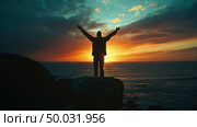 A man is standing confidently on a large rock overlooking the ocean, with waves crashing below him. Стоковое AI-изображение, AI-художник Данила Большаков / Фотобанк Лори