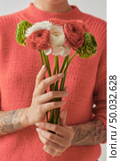 A girl with a tattoo is holding a bouquet of different flowers Ranunculus on a white background. Congratulation card concept. Trend color of the year 2019 Living Coral Pantone.. Young girl in a sweater in a color of the year 2019 Living Coral Pantone holding a bouquet of fresh flowers in her hands with tatoo. Стоковое фото, агентство Ingram Publishing / Фотобанк Лори