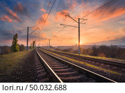 Railroad against beautiful sky at sunset. Industrial landscape with railway station, colorful blue sky with red  clouds, trees and green grass, yellow sunlight. Railway junction. Heavy industry. Стоковое фото, агентство Ingram Publishing / Фотобанк Лори