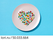Many different pills and supplements in a shape of a heart on a white plate on a blue background. Cardiovascular disease prevention. Flat lay. Heart made from medicine pills and capsules on a white plate on a blue background, copy space. Colorful food supplement pills. Top view. Стоковое фото, агентство Ingram Publishing / Фотобанк Лори
