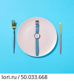 Watch with time six o’clock on a white plate with knife and fork on a blue background, place for text. Concept of limiting the intake of food diet and weight loss. Flat lay.. White plate with whatch shows six o’clock served knife and fork on a blue background and shadows. Time to eat and diet concept. Top view. Стоковое фото, агентство Ingram Publishing / Фотобанк Лори