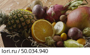 Watering of fresh organic tropical fruits in a box- ananas, mango, passion, orange on a wooden background. Panoramic motion, 4K UHD video, 3840, 2160p.. Droplets water on a fresh juicy exotic fruits in a box on a wooden table. Panoramic motion, 4K UHD video, 3840, 2160p. Стоковое фото, агентство Ingram Publishing / Фотобанк Лори