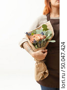 Summer wonderful fresh roses, eryngium and green leaves as a greeting bunch in a female’s hand with tattoo on a light background. Place for text. Gift for Mother’s or Woman’s Day.. Woman with red hair holds beautiful colourful blossoming flower bouquet of fresh roses living coral color on a white background. Copy space. Mother’s Day. Стоковое фото, агентство Ingram Publishing / Фотобанк Лори