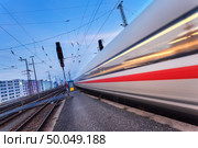 High speed passenger train on railroad track in motion at night. Blurred commuter train. Railway station at twilight in Nuremberg, Germany. Railroad travel, railway tourism. Industrial landscape. Стоковое фото, агентство Ingram Publishing / Фотобанк Лори