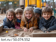 Five happy children playing in a sandbox outdoors. They are all dressed in warm winter clothes, and their faces are glowing with happy smiles. The children are digging in the sand, several toys are visible around. In the background are blurred elements of the playground and an autumn-winter landscape. The photo conveys the atmosphere of children's friendship, freedom, natural fun and comfort. Suitable for themes: childhood, active games, walks, upbringing, preschool education, healthy lifestyle. Стоковое AI-изображение, AI-художник Анна Кривицкая / Фотобанк Лори